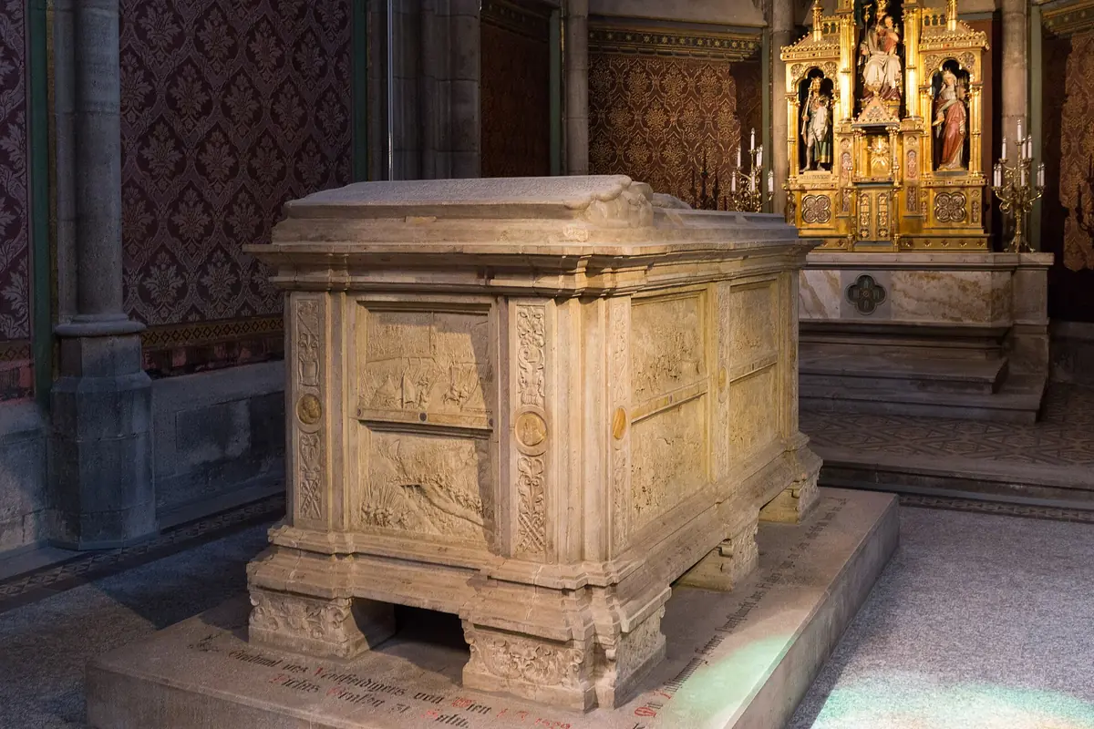 The sandstone tomb of Count Nicholas of Salm in a side chapel, with relief carving and a gilded altar behind it.