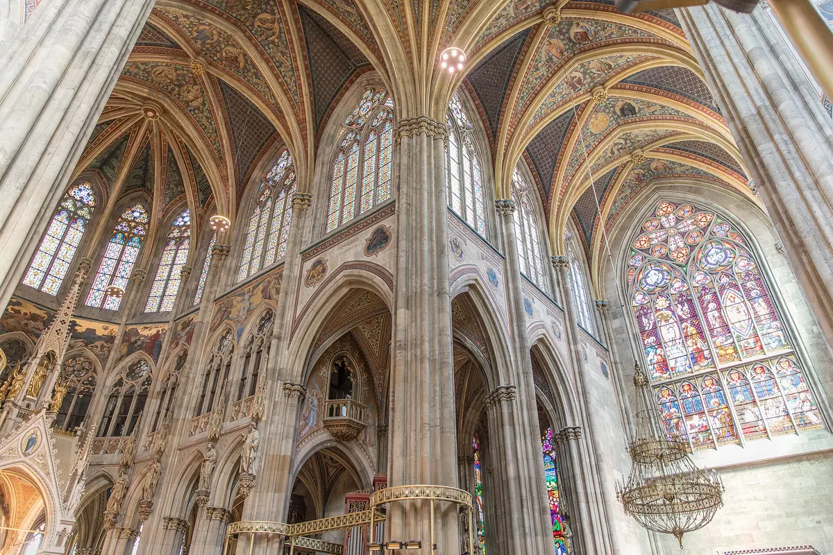 Looking up inside the Votivkirche at cream-coloured ribbed vaults, tall pointed windows and a large stained-glass rose window on the right.